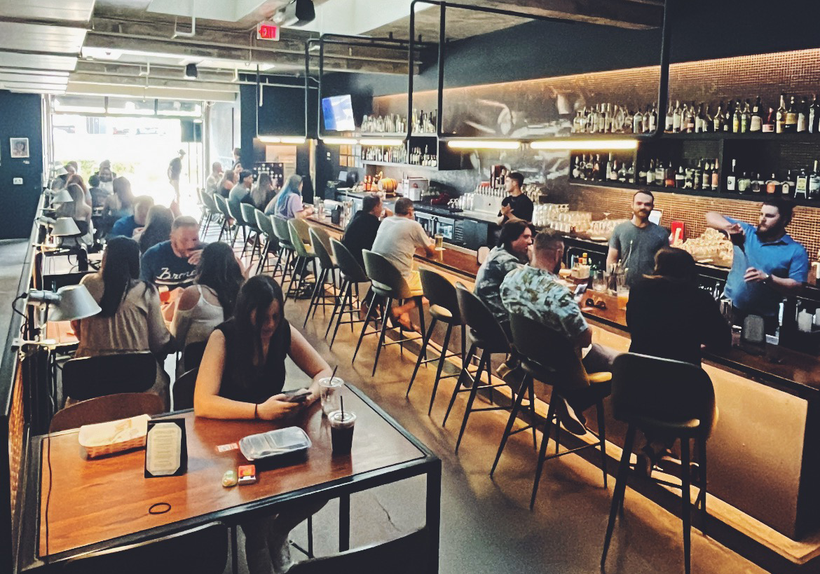 People siting at tables and the bar while bartenders serve drinks.